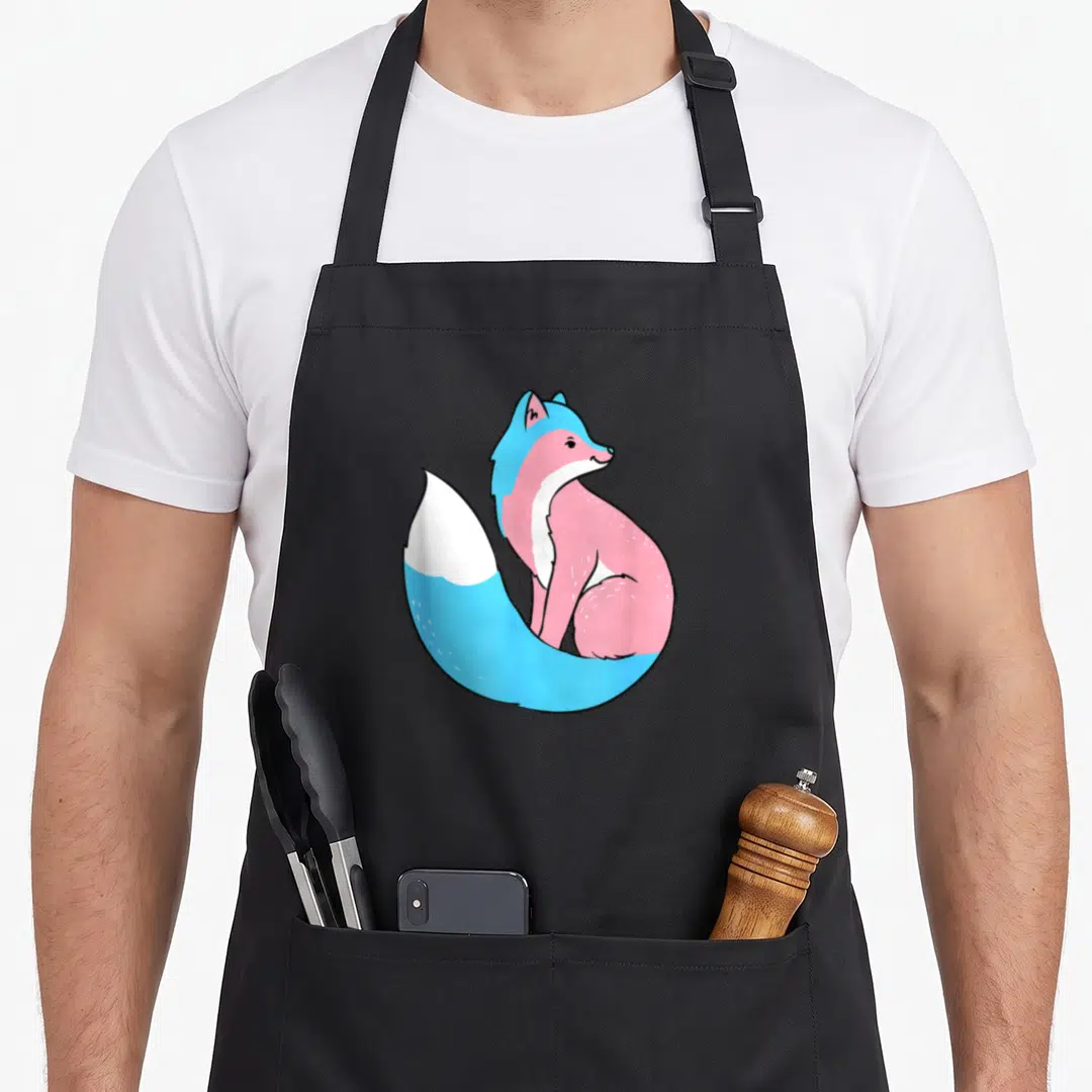 Tran fox print apron - Cartoon fox in blue pink and white transgender pride colors — shown on a black cotton canvas apron against a white background