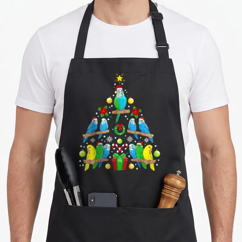 Christmas birds apron - Cartoon budgies perched on branches forming a Christmas tree shape with star and gift box — shown on a black cotton canvas apron against a white background