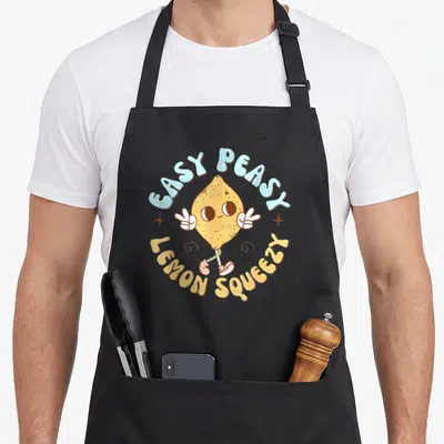 Peasy lemon apron - Retro cartoon lemon character with peace signs and arched text EASY PEASY LEMON SQUEEZY in yellow — shown on a black cotton canvas apron against a white background