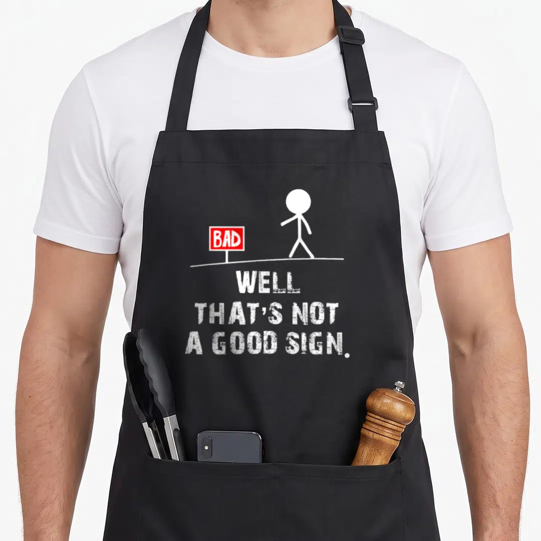Well sarcastic apron - Stick figure walks past red bad sign above white text well that's not a good sign — shown on a black cotton canvas apron against a white background