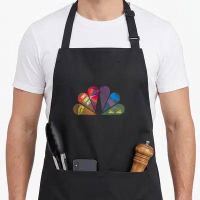 Mash comfortable nbc apron - Stylized NBC logo heart shape with overlapping red blue yellow purple and green petals — shown on a black cotton canvas apron against a white background