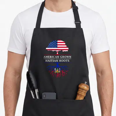 Grown birthday prince apron - Tree with US flag canopy and Haiti flag roots separated by text AMERICAN GROWN — shown on a black cotton canvas apron against a white background