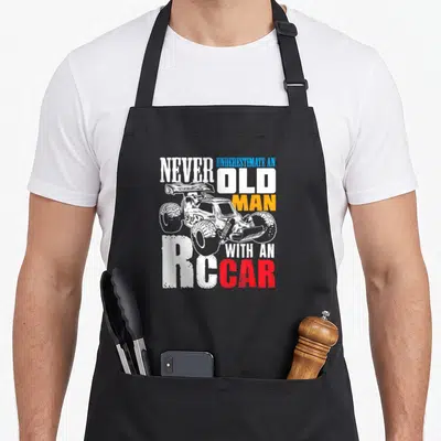 Racing racer car apron - Distressed RC monster truck graphic with white blue orange and red text — shown on a black cotton canvas apron against a white background