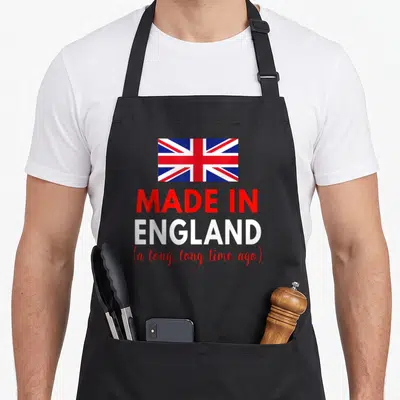 Funny ago birthday apron - Union Jack flag above red and white text reading Made in England a long long time ago — shown on a black cotton canvas apron against a white background