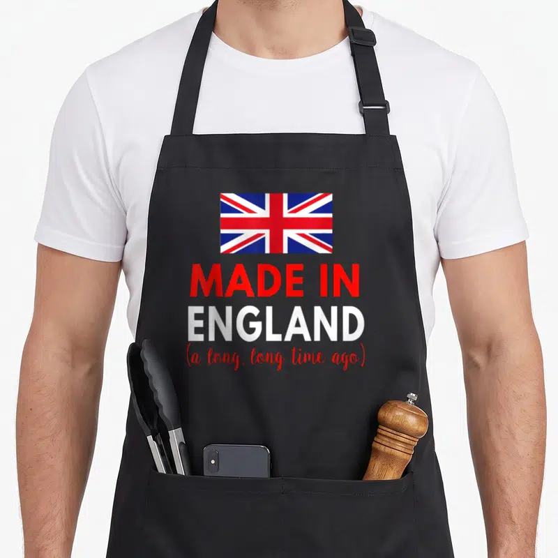 Funny ago birthday apron - Union Jack flag above red and white text reading Made in England a long long time ago — shown on a black cotton canvas apron against a white background