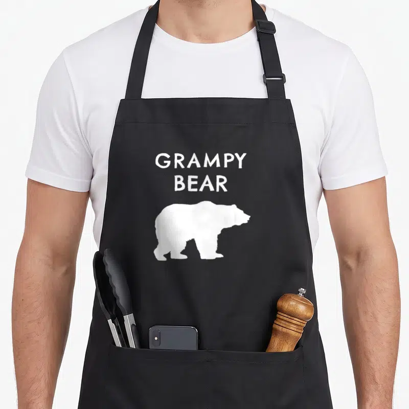 Grampy bear apron - Stacked white GRAMPY BEAR text above a white bear silhouette on dark background — shown on a black cotton canvas apron against a white background