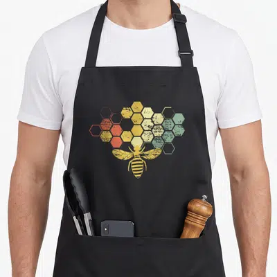 Funny beekeeper honey bee apron - Retro bee over honeycomb cells with orange yellow and green gradient — shown on a black cotton canvas apron against a white background