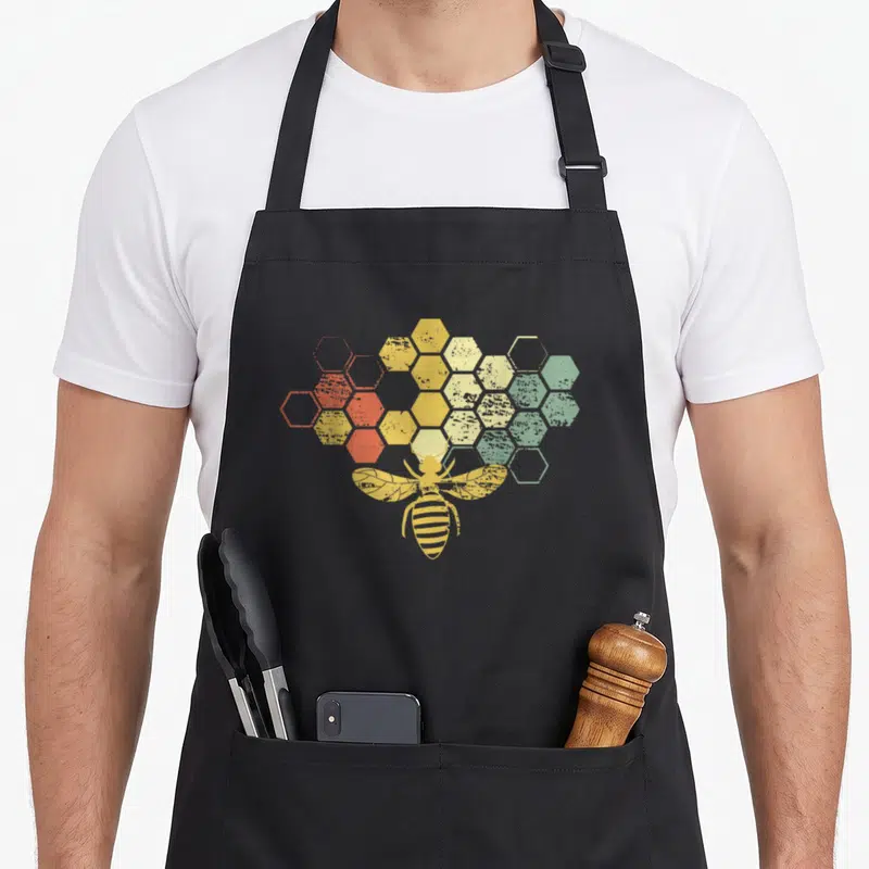 Funny beekeeper honey bee apron - Retro bee over honeycomb cells with orange yellow and green gradient — shown on a black cotton canvas apron against a white background