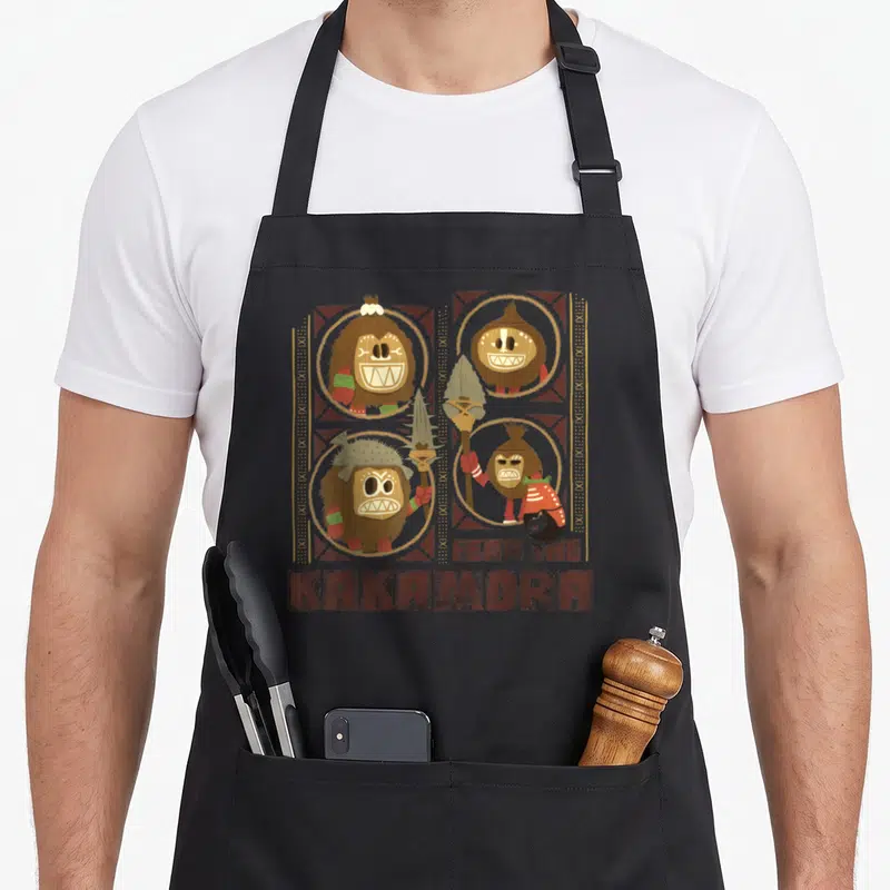Fear tiki aprons - Three brown and tan coconut warriors in circles with Fear the Kakamora text and tribal borders — shown on a black cotton canvas apron against a white background