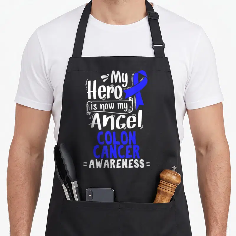 Colorectal patient apron - Blue ribbon and stacked text My Hero is now my Angel Colon Cancer Awareness — shown on a black cotton canvas apron against a white background