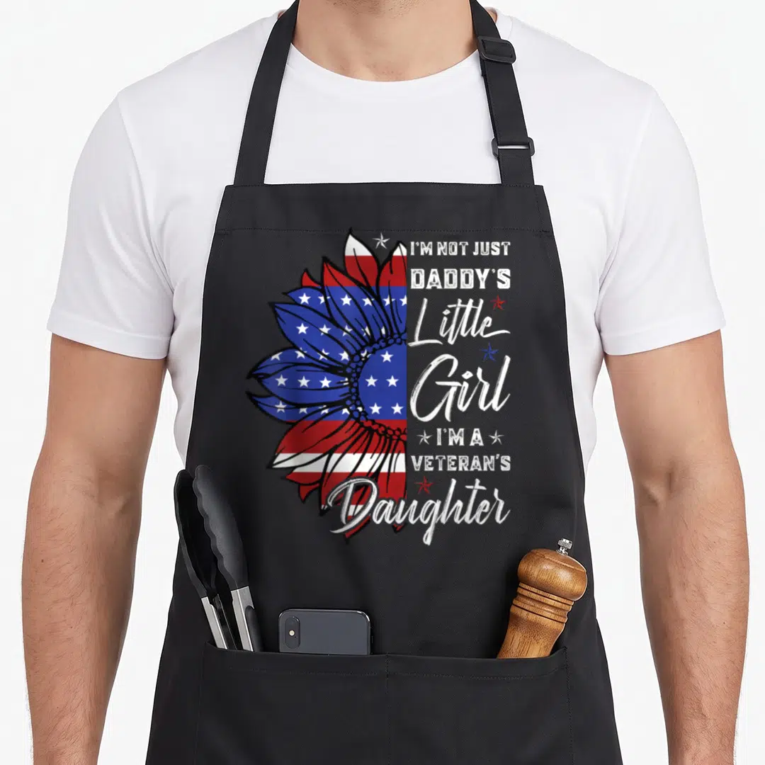 Veteran daddy daughter apron - Patriotic sunflower filled with US flag pattern and stacked text reading I'm a Veteran's — shown on a black cotton canvas apron against a white background