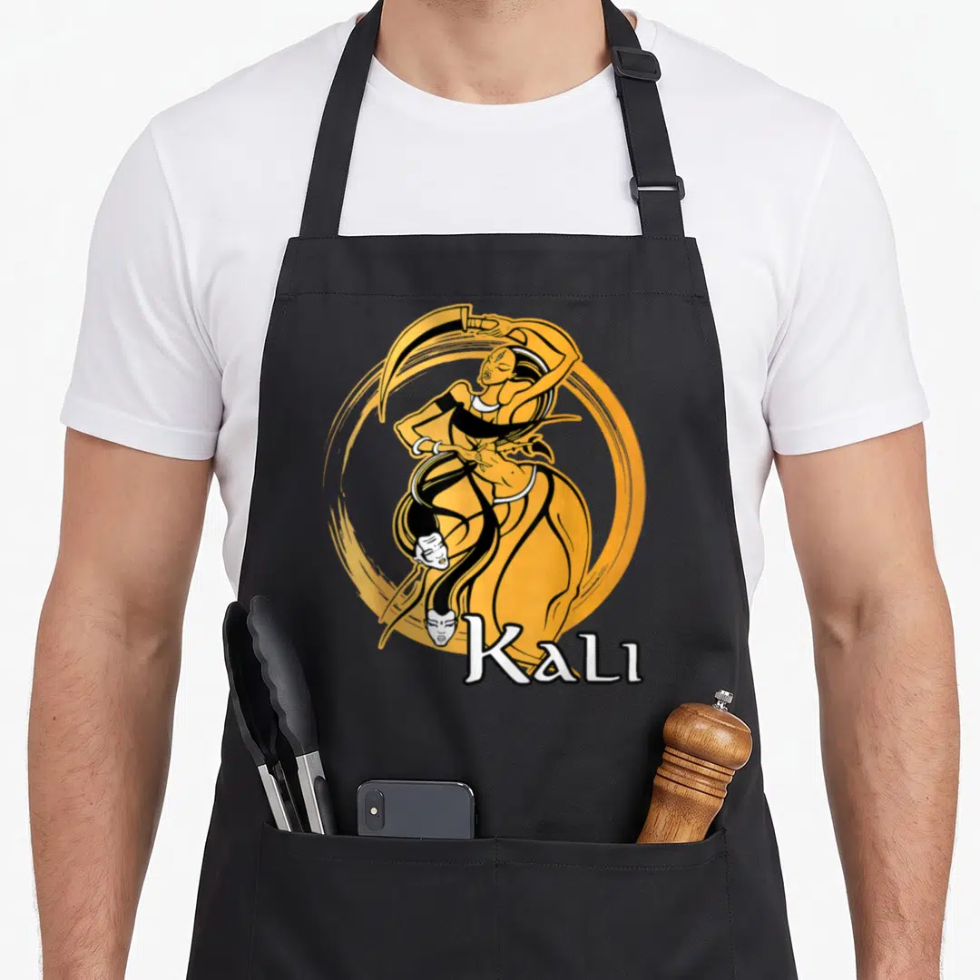 Goddess diwali apron - Cartoon Kali holding scythe in orange circle with text label — shown on a black cotton canvas apron against a white background