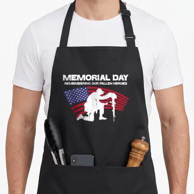 Remembering patriotic apron - Kneeling soldier silhouette over waving flag with MEMORIAL DAY text in distressed white — shown on a black cotton canvas apron against a white background