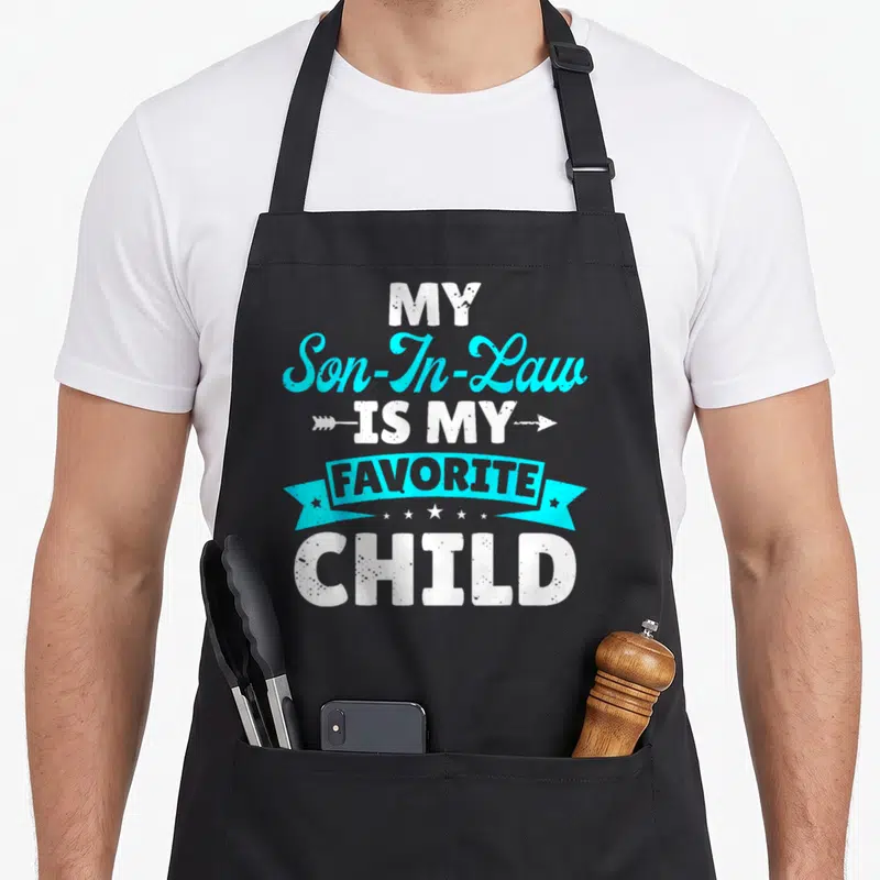 Law family aprons - White and cyan stacked text reading My Son In Law Is My Favorite Child with an arrow and ribbon — shown on a black cotton canvas apron against a white background