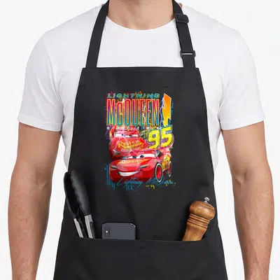 Thunder car apron - Lightning McQueen Racing 95 text with two red cars yellow bolt and script signature in cartoon style — shown on a black cotton canvas apron against a white background