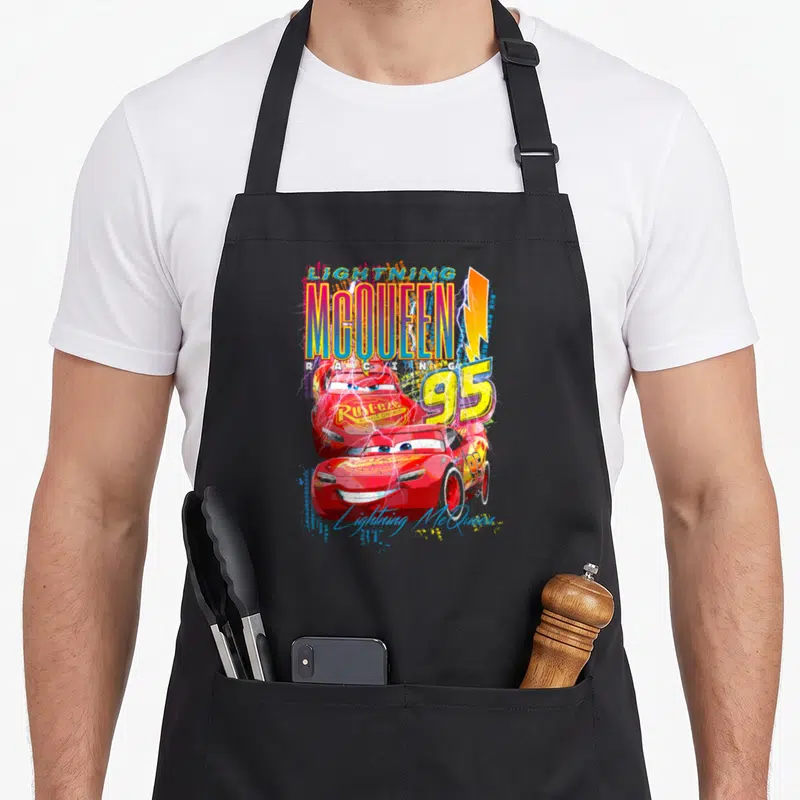 Thunder car apron - Lightning McQueen Racing 95 text with two red cars yellow bolt and script signature in cartoon style — shown on a black cotton canvas apron against a white background