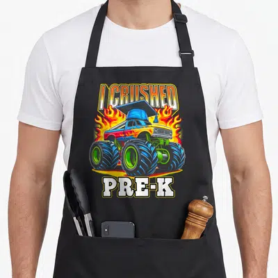 Grad truck apron - Blue monster truck with graduation cap surrounded by flames and text I CRUSHED PRE-K — shown on a black cotton canvas apron against a white background