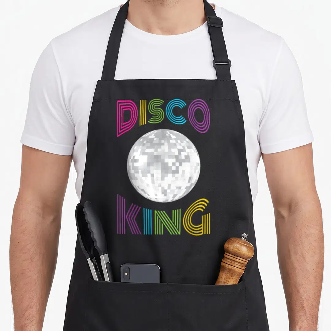 70s king apron - Disco ball centered between arched DISCO and KING text in multi-colored striped letters — shown on a black cotton canvas apron against a white background