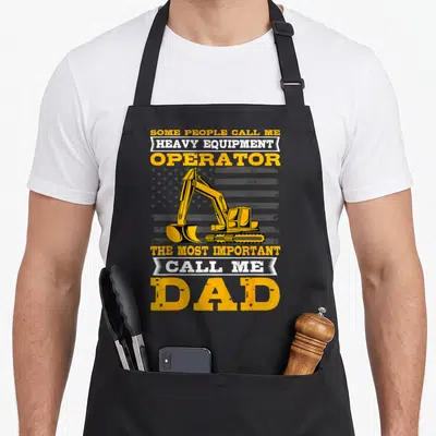 Father heavy canvas aprons - Yellow excavator over distressed flag with dad and operator text — shown on a black cotton canvas apron against a white background