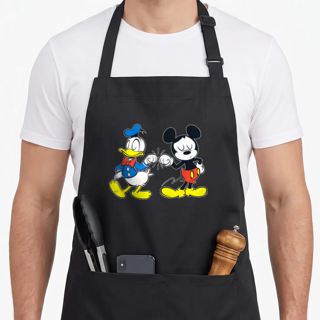 Outline duck apron - Donald Duck and Mickey Mouse bumping fists in blue, yellow, red, black, and white cartoon style — shown on a black cotton canvas apron against a white background