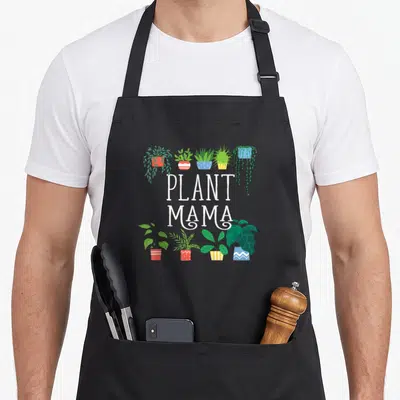 Plant mama apron - PLANT MAMA text with five top and four bottom potted plants in cartoon style — shown on a black cotton canvas apron against a white background