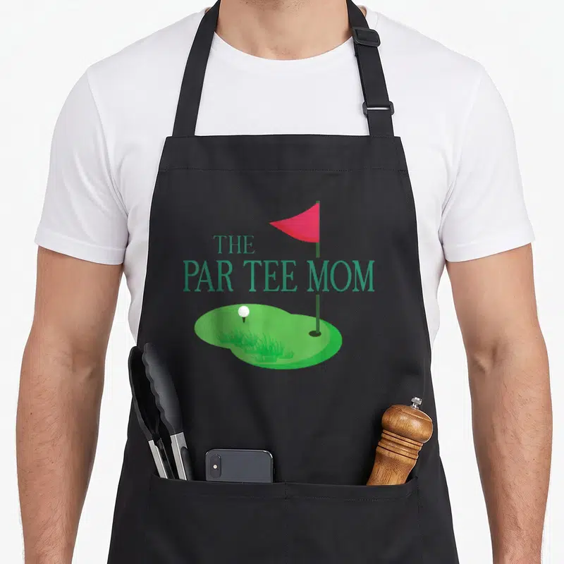 Parent golf apron - THE PAR TEE MOM text over red flag and green putting surface with white ball — shown on a black cotton canvas apron against a white background