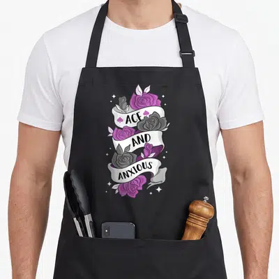 Ace rose apron - Purple and grey roses with white ribbon reading ACE AND ANXIOUS — shown on a black cotton canvas apron against a white background