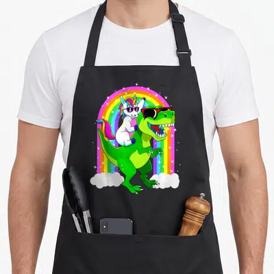 Riding trex dinosaur apron - Cartoon unicorn and t-rex with sunglasses under rainbow arch with stars — shown on a black cotton canvas apron against a white background