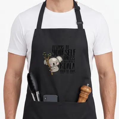 Koala always yourself apron - Cartoon koala hugging brown branch next to six lines of black text — shown on a black cotton canvas apron against a white background
