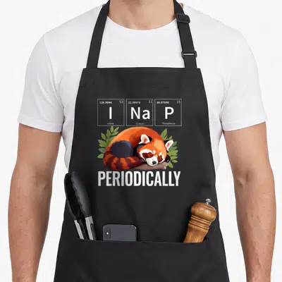Nap animal apron - Sleeping red panda below I Na P periodic table cells with green leaves and PERIODICALLY text — shown on a black cotton canvas apron against a white background