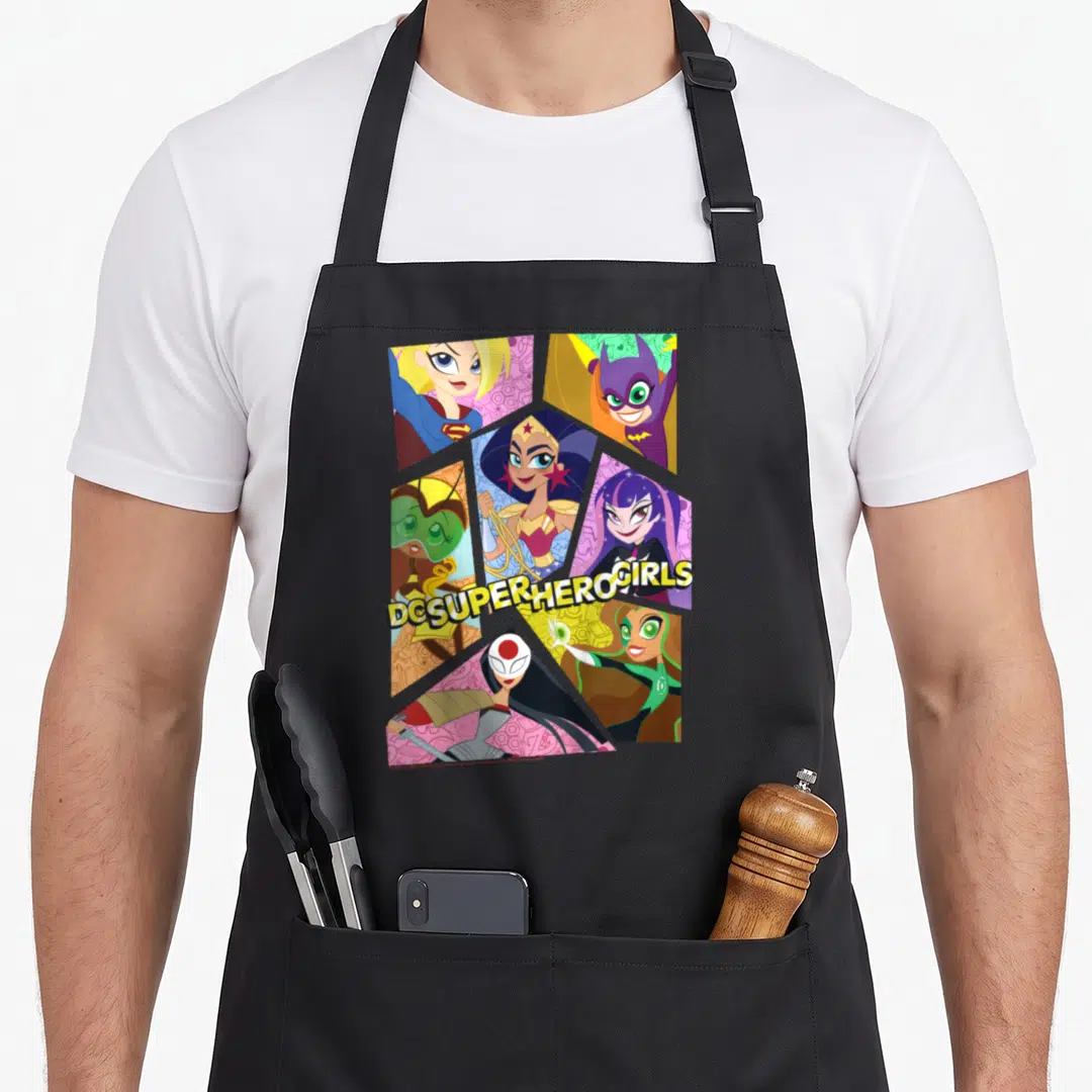 Collage super hero aprons - Six cartoon superhero girls in honeycomb layout with DC SUPER HERO GIRLS text — shown on a black cotton canvas apron against a white background