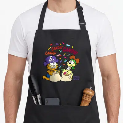 Candy cat apron - Garfield and Odie in pirate hats holding candy bags under CANDY text arch with orange and purple — shown on a black cotton canvas apron against a white background