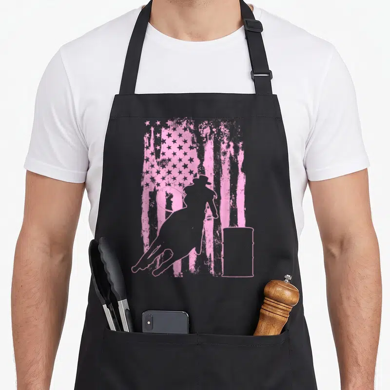 Barrel american flag apron - Grey rider outline and barrel over distressed pink flag stripes and stars — shown on a black cotton canvas apron against a white background