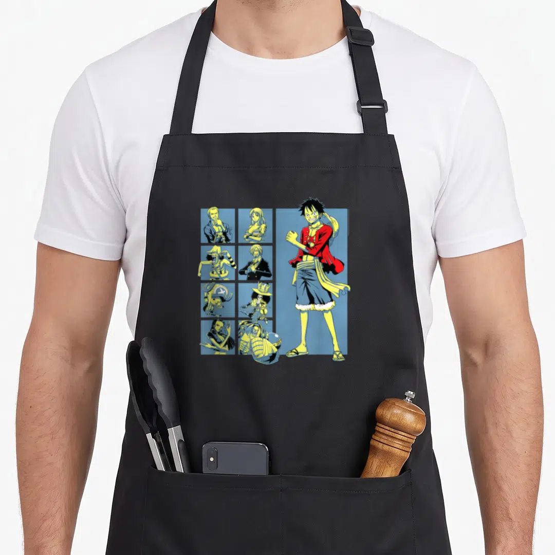 Pirate anime character apron - Luffy stands right of eight crew portraits in blue squares using red, yellow, and blue — shown on a black cotton canvas apron against a white background