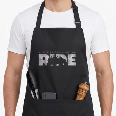 Quad road apron - LIFE IS BETTER WHEN YOU RIDE text with off-road vehicle silhouette in distressed white brown grey — shown on a black cotton canvas apron against a white background