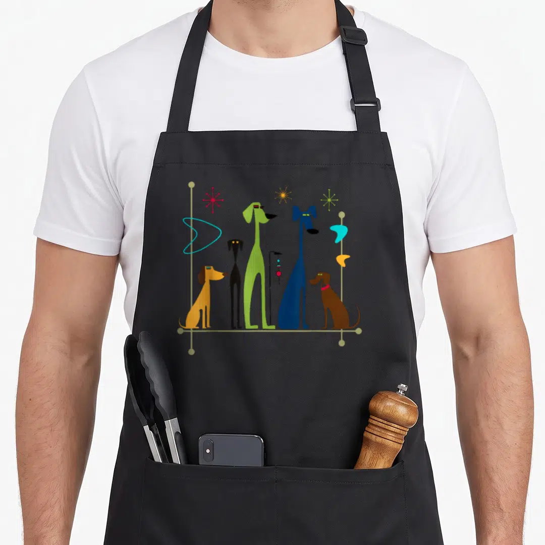Century modern apron - Five stylized dogs in orange, black, green, blue, and brown standing in a row with starbursts — shown on a black cotton canvas apron against a white background