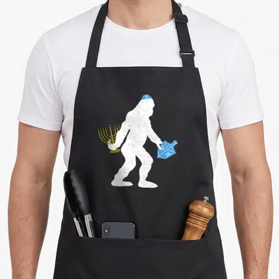 Bigfoot hanukkah apron - White Bigfoot silhouette holding gold menorah and blue dreidel with distressed texture — shown on a black cotton canvas apron against a white background