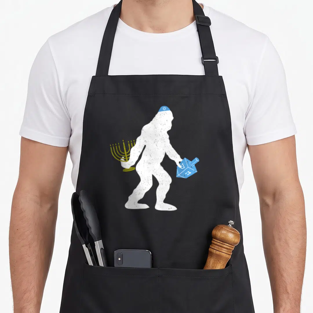 Bigfoot hanukkah apron - White Bigfoot silhouette holding gold menorah and blue dreidel with distressed texture — shown on a black cotton canvas apron against a white background