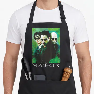 Neo character aprons - Three characters in sunglasses below THE MATRIX text on green background — shown on a black cotton canvas apron against a white background
