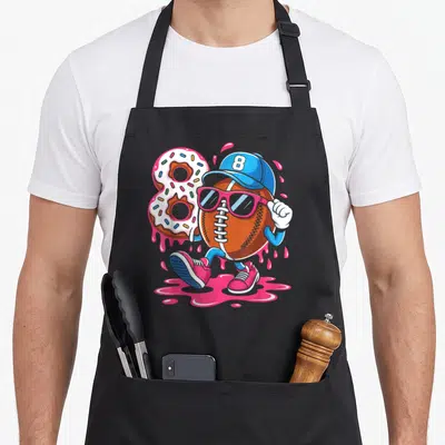Football ice cream apron - Walking football character with sunglasses next to number 8 donut and pink splashes — shown on a black cotton canvas apron against a white background