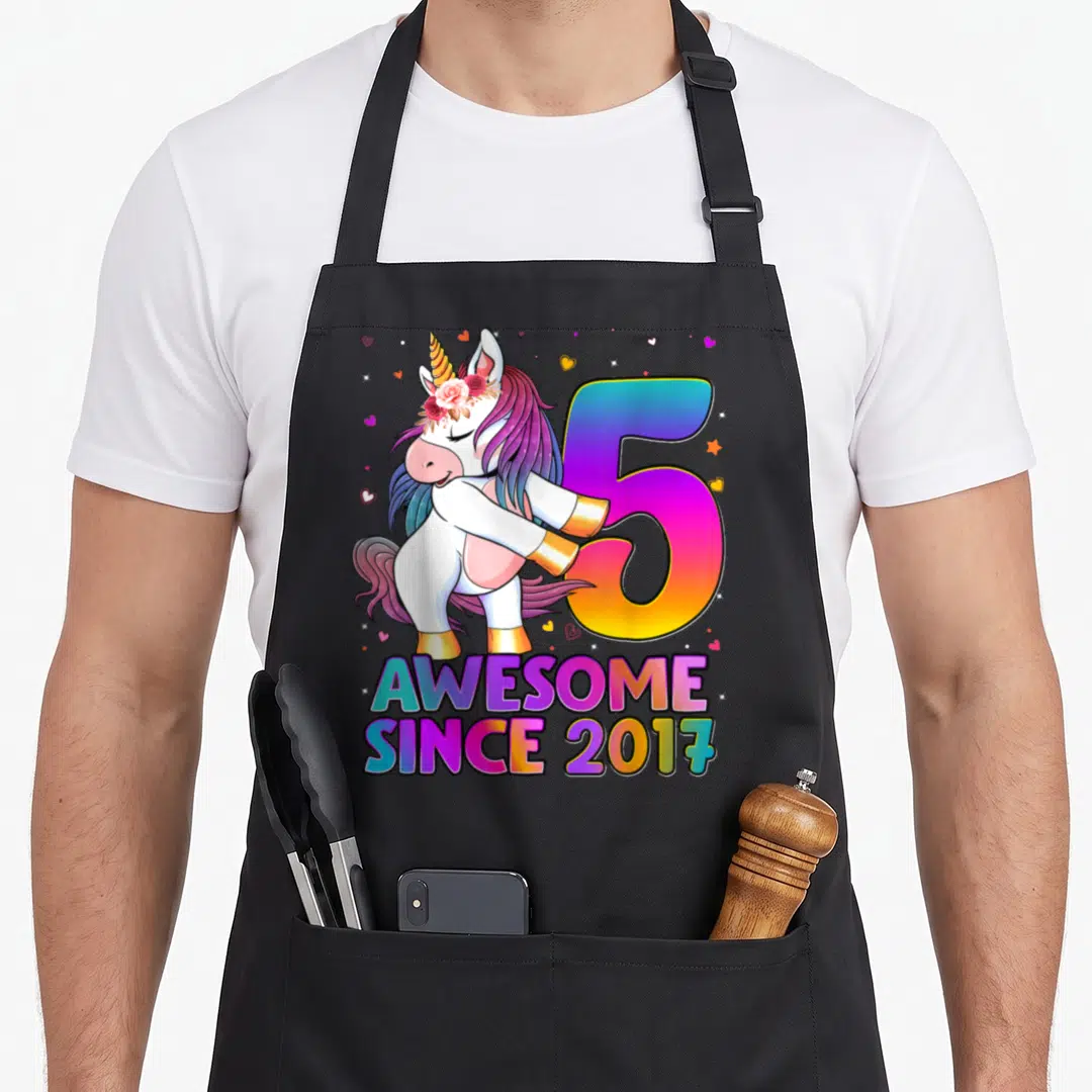 5th unicorn apron - Cartoon unicorn dabbing next to number 5 and AWESOME SINCE 2017 text — shown on a black cotton canvas apron against a white background