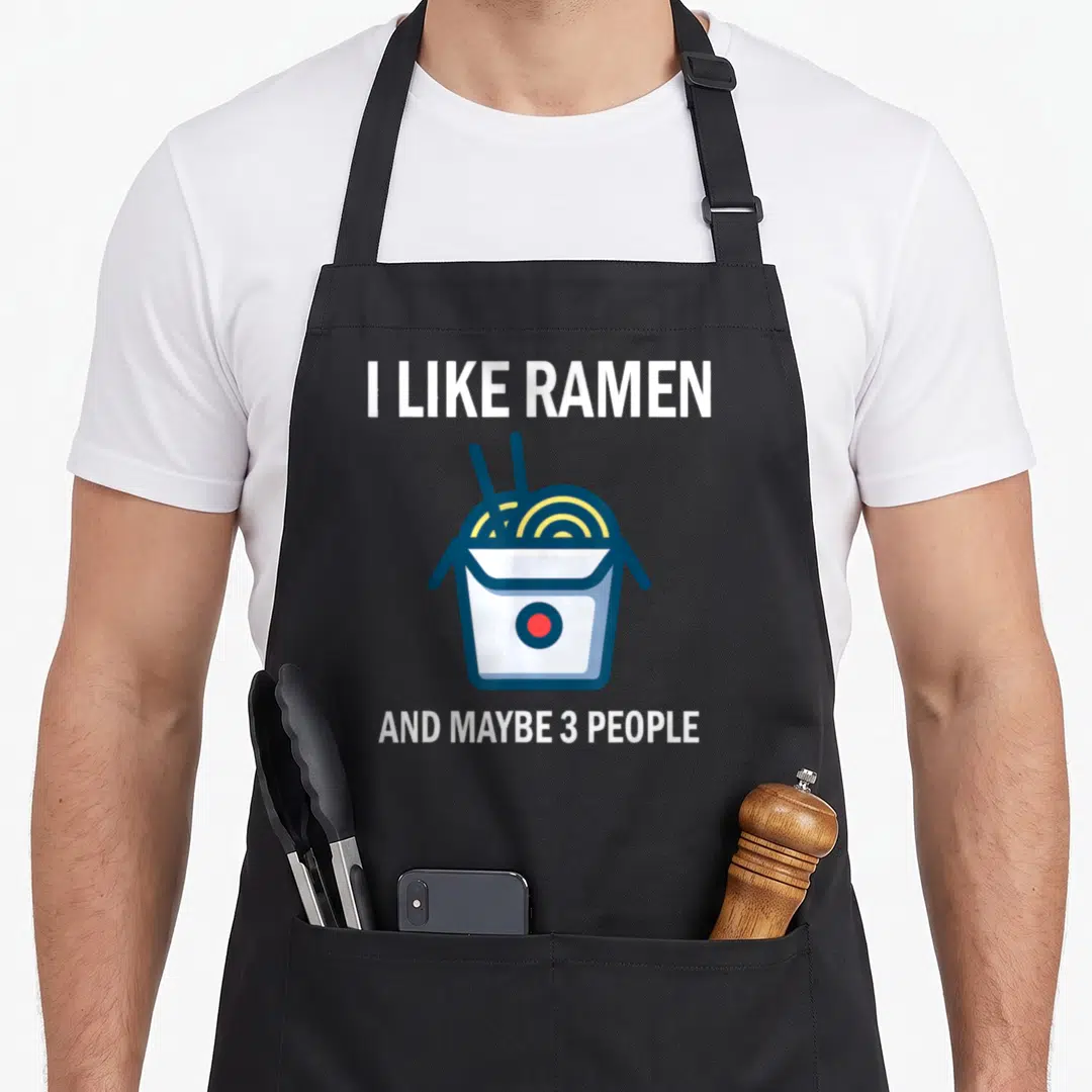 Food anime apron - I like ramen and maybe 3 people text with takeout box graphic — shown on a black cotton canvas apron against a white background