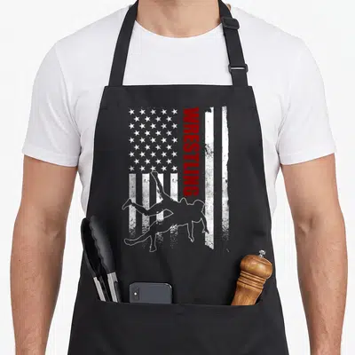 Funny flag wrestling apron - Vertical WRESTLING text beside two wrestler silhouettes on distressed flag — shown on a black cotton canvas apron against a white background
