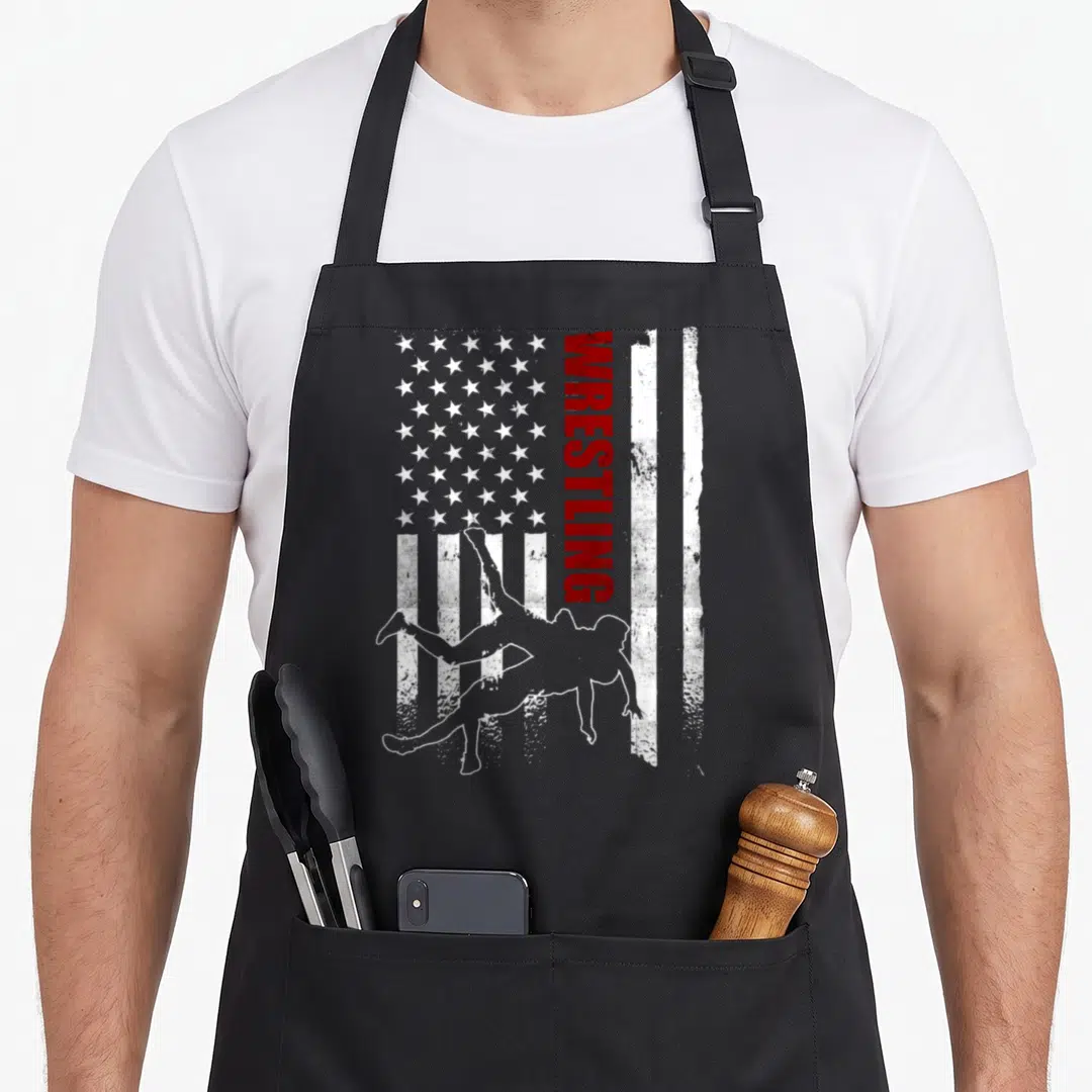 Funny flag wrestling apron - Vertical WRESTLING text beside two wrestler silhouettes on distressed flag — shown on a black cotton canvas apron against a white background