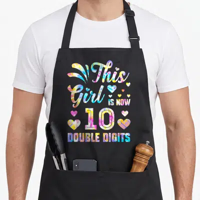 Birthday tie-dye apron - This Girl IS NOW 10 DOUBLE DIGITS tie-dye text with hearts in pink blue yellow purple — shown on a black cotton canvas apron against a white background