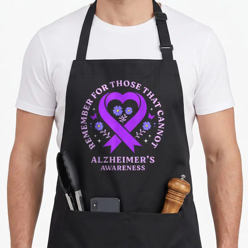 Remember alzheimer's aprons - Purple heart ribbon with blue flowers and stars, text: Remember For Those That Cannot — shown on a black cotton canvas apron against a white background