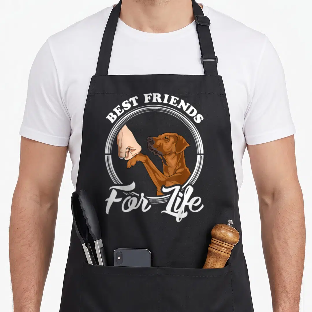 Cool rhodesian ridgeback apron - Brown dog fist bumping human hand in white circle with best friends for life text — shown on a black cotton canvas apron against a white background