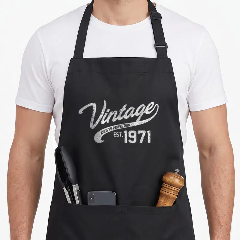 47th birthday apron - White distressed text reading Vintage Aged to Perfection EST 1971 on black background — shown on a black cotton canvas apron against a white background
