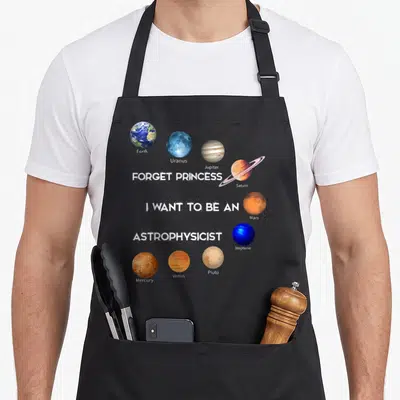 Retro forget princess apron - Planets including Saturn and Mars surround stacked white text reading Forget Princess I — shown on a black cotton canvas apron against a white background