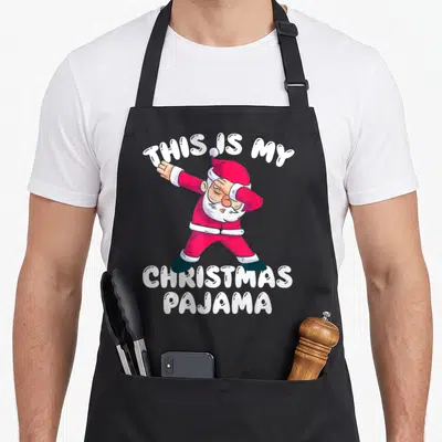 Pajamas christmas santa apron - Dabbing Santa with THIS IS MY CHRISTMAS PAJAMA text in red white pink — shown on a black cotton canvas apron against a white background